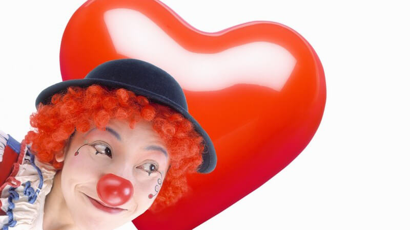 Mann als Clown geschminkt, dahinter rotes Herz auf weißem Hintergrund
