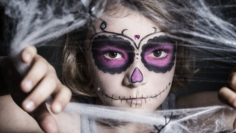 Dunkel geschminktes Mädchen guckt durch ein künstliches Spinnennetz zu Halloween