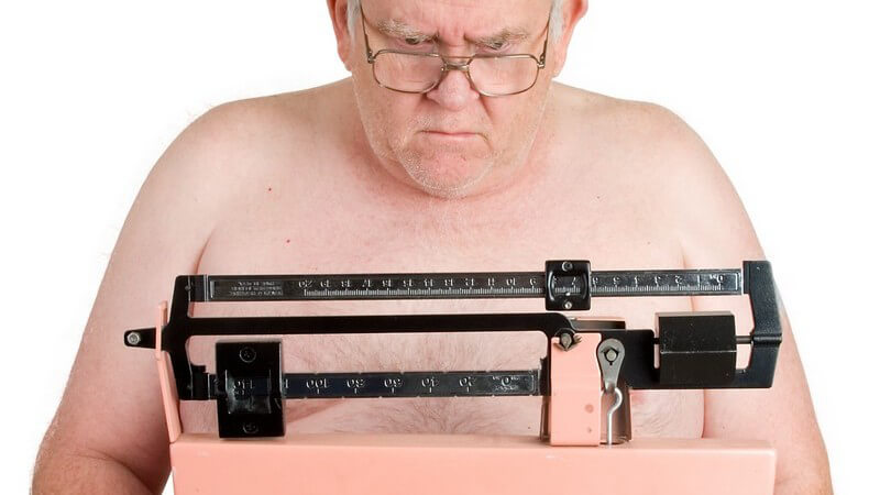 Älterer Mann mit Brille und Halbglatze steht mit nacktem Oberkörper auf einer alten Waage