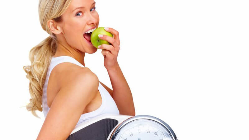 Junge Frau beisst in grünen Apfel, trägt Waage