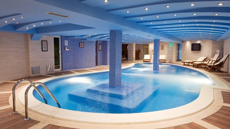 Luxus Pool mit Säulen in Raum mit Liegestühlen aus Holz unter beleuchteter Decke