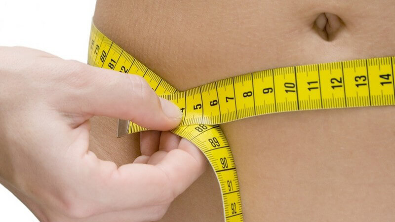 Abnehmen - Frau misst sich mit Maßband den Bauchumfang