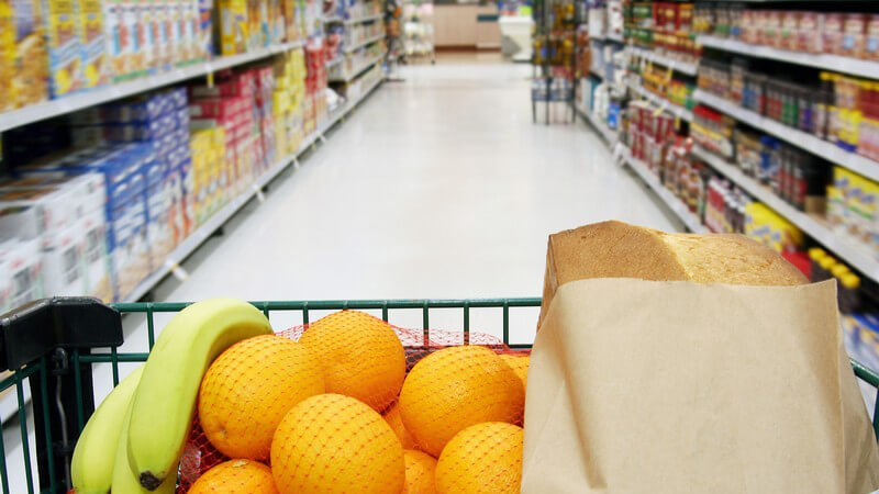 Einkaufswagen mit frischen Obst wird durch Gang im Supermarkt geschoben