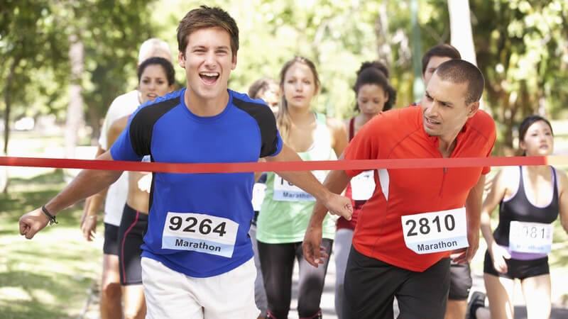 Marathonläufer in blauem Trikot kommt als erster durchs Ziel, Läufer in rotem Trikot hat das Nachsehen