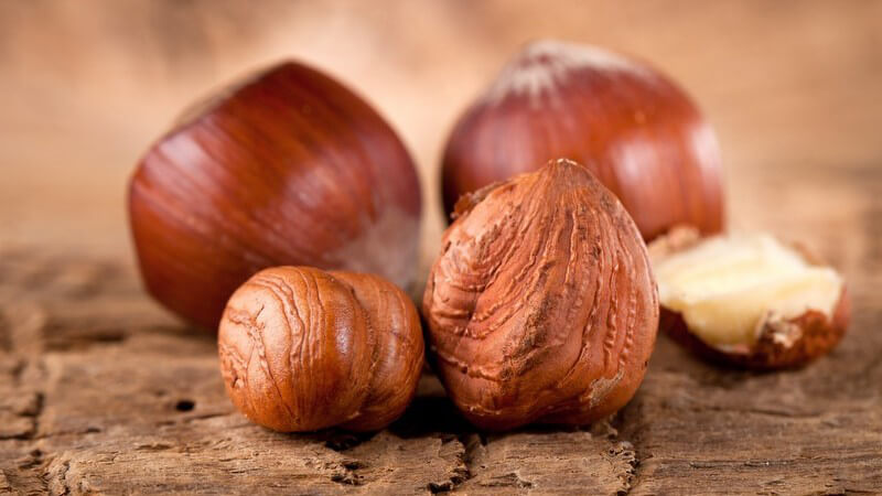 Zwei Haselnüsse mit und ohne Schale auf rustikalem Holz