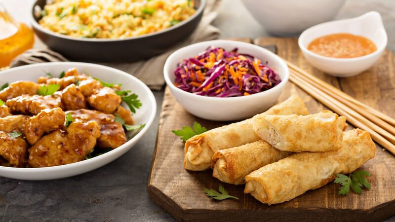 Frühlingsrollen neben Essstäbchen und Rotkraut auf Holzbrett