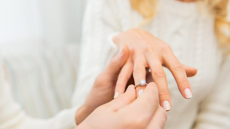 Mann streift einer blonden Frau einen Diamantring über den Finger