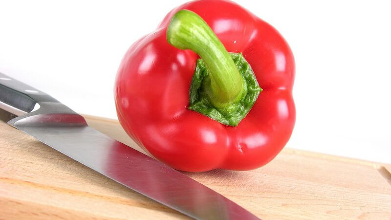 Frische, rote Paprika neben scharfem Messer auf Holzbrett