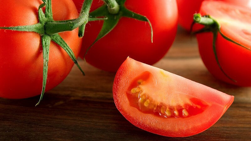 Frische Tomaten, ganz und aufgeschnitten auf Holzuntergrund