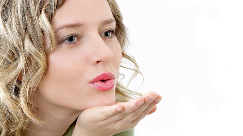 Blonde Frau mit lockigen Haaren macht Kussmund und pustet Kuss zur Seite