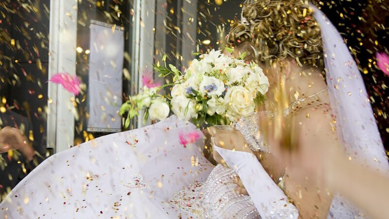 Braut mit Brautstrauß wird mit goldenem Konfetti beworfen