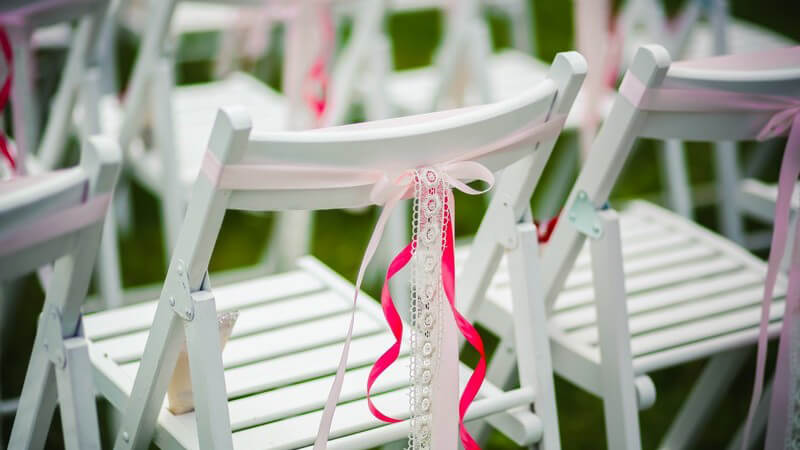 Weiße Holzstühle mit rosanen Schleifen für Hochzeitsgäste - Hochzeitsdekoration