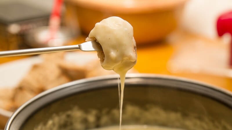 Käse-Fondue: Stück Brot mit geschmolzenem Käse wird aus dem Fonduetopf geholt