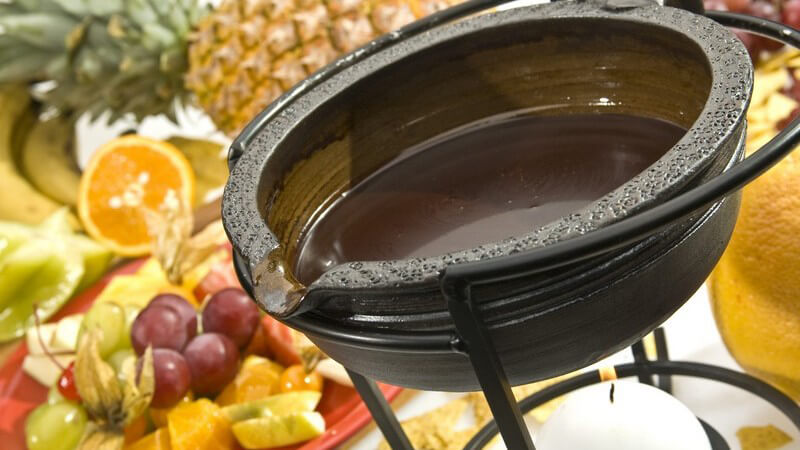 Schoko-Fondue, frisches Obst liegt neben Fondueschale mit flüssiger Schokolade