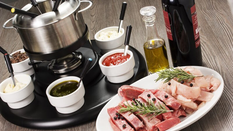 Fondue-Set mit Zutaten: Fleisch und verschiedene Dips, dazu ein Rotwein