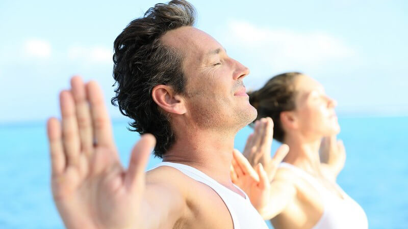 Paar in weißen Oberteilen macht Yoga-Übungen am Meer