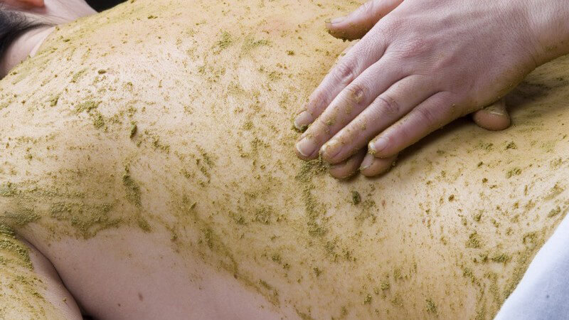 Nahaufnahme Rücken eines Mannes bei Ayurvedamassage mit grüner Masse