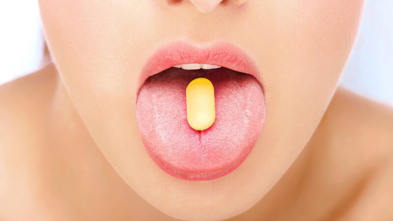 Nahaufnahme ausgestreckte Zunge einer Frau mit gelber Tablette darauf