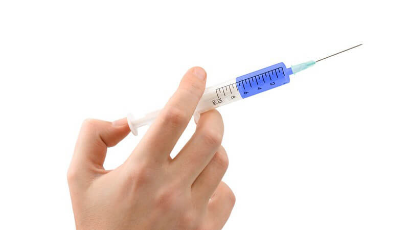 Frauenhand hält eine weiß-blaue Spritze, Daumen am Kolben