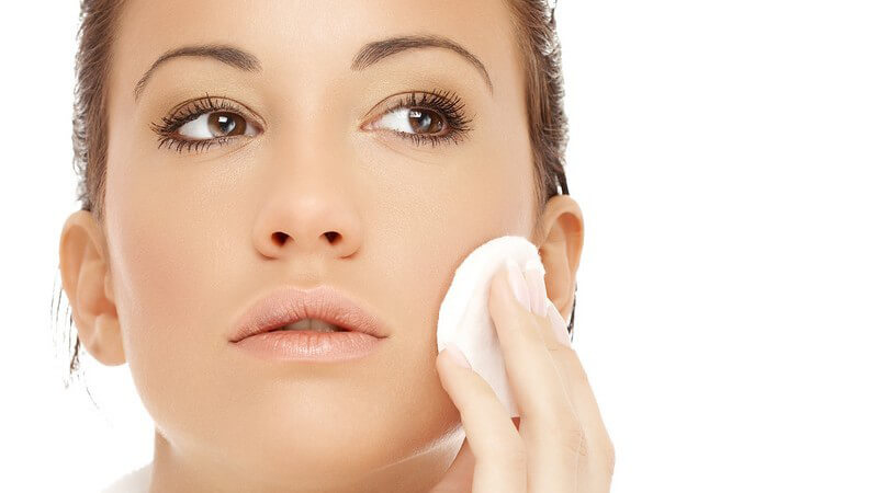 Junge, dunkelhaarige Frau mit Wattepad beim Abschminken