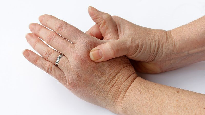 Ältere Frau umgreift ihre linke Hand wegen Gelenkschmerzen oder Gicht, weißer Hintergrund