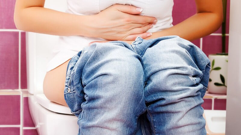 Frau auf Toilette, hält sich den Bauch, Bauchschmerzen, Durchfall