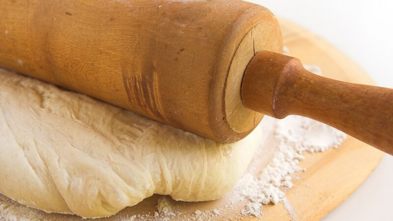 Teig auf mehligem Holzbrett, darauf Teigroller aus Holz