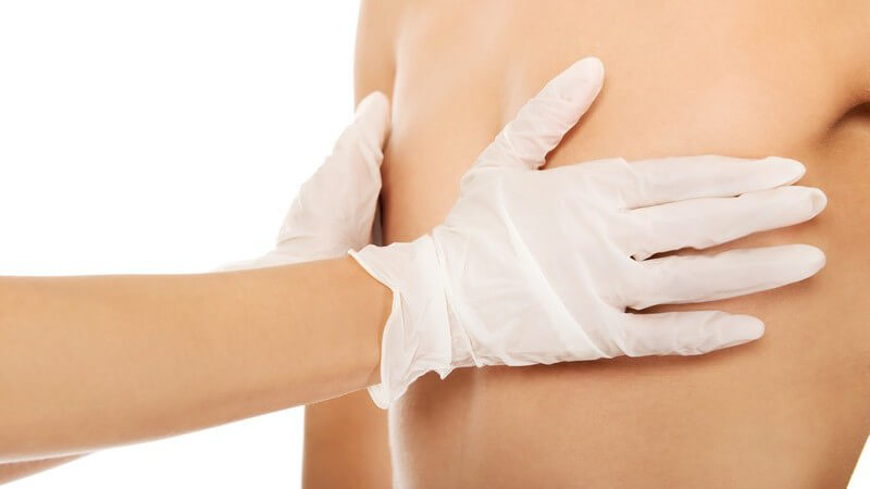 Chirurgenhände in Schutzhandschuhen liegen auf den Brüsten einer Frau vor einer Brustoperation