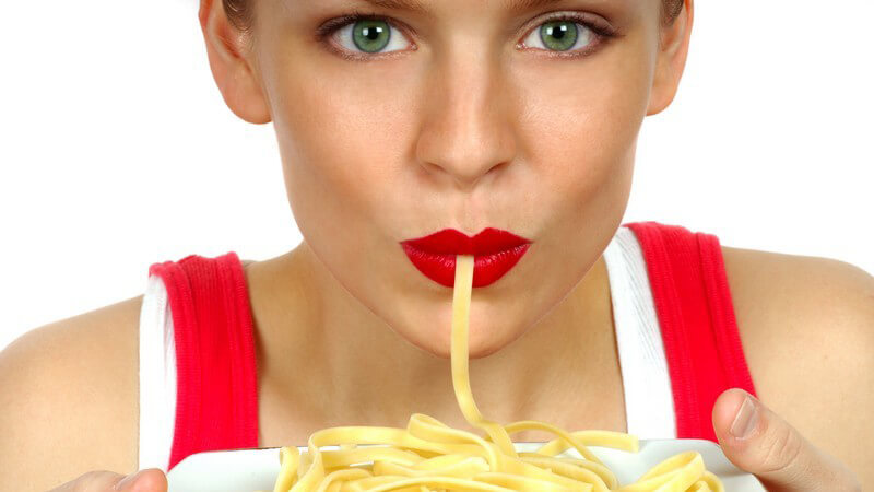 Frau mit rotem Lippenstift hält einen Pastateller hoch und saugt an einer Nudel