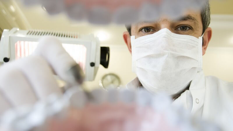 Zahnarzt mit Mundschutz bei Zahnuntersuchung