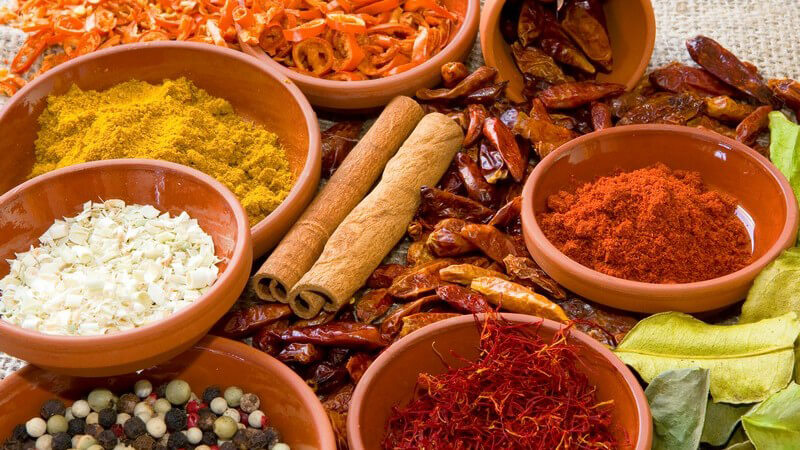 Gewürze in Tonschalen, im Zentrum 2 Zimtstangen auf getrockneten Chilischoten