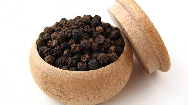 Schwarzer Pfeffer in kleiner Holzdose, daneben Deckel