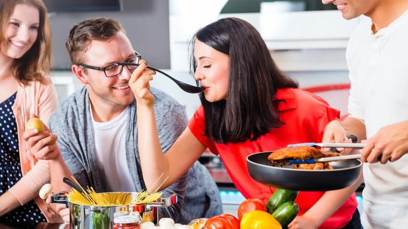 Vier Freunde beim gemeinsamen Kochen von Pasta und Fleisch