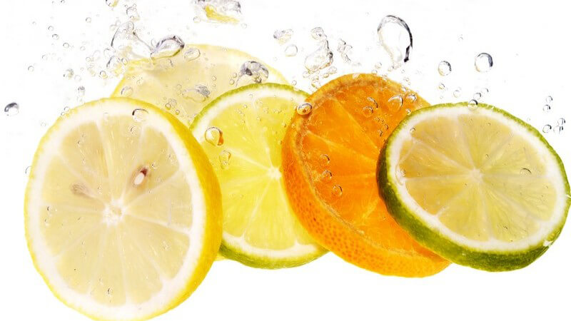 Scheiben von Zitrusfrüchten werden ins Wasser geworfen, bilden Luftbläschen