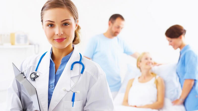 Junge Ärztin im Vordergrund, Patientin mit Freund und Krankenschwester im Hintergrund