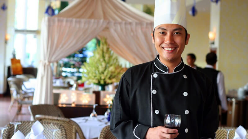 Chefkoch in schwarzer Kochkleidung mit Glas Rotwein im Restaurant