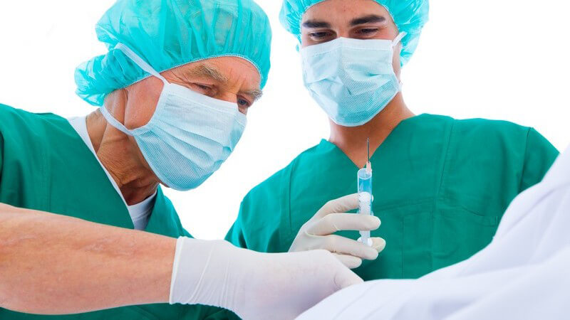 Zwei Chirurgen mit grünem Kittel und Mundschutz mit Spritze