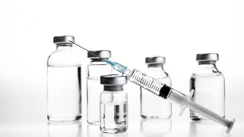 Fünf Glasfläschchen in verschiedenen Größen und eine Spritze