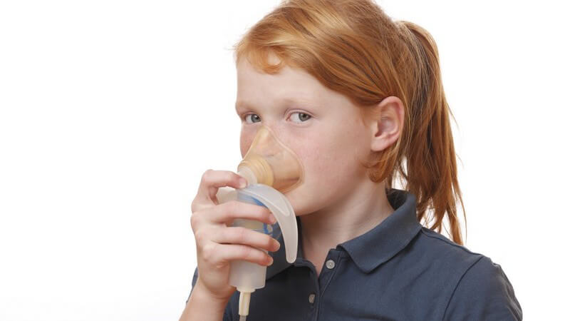 Mädchen mit roten Haaren inhaliert aus einem Inhalationsgerät, weißer Hintergrund
