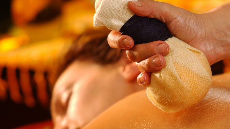 Pantai Luar Massage mit Kräuterstempel auf Rücken einer Frau