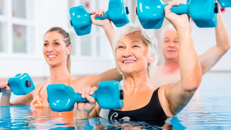 Junge Frau und ein älteres Paar bei der Wassergymnastik mit blauen Hanteln