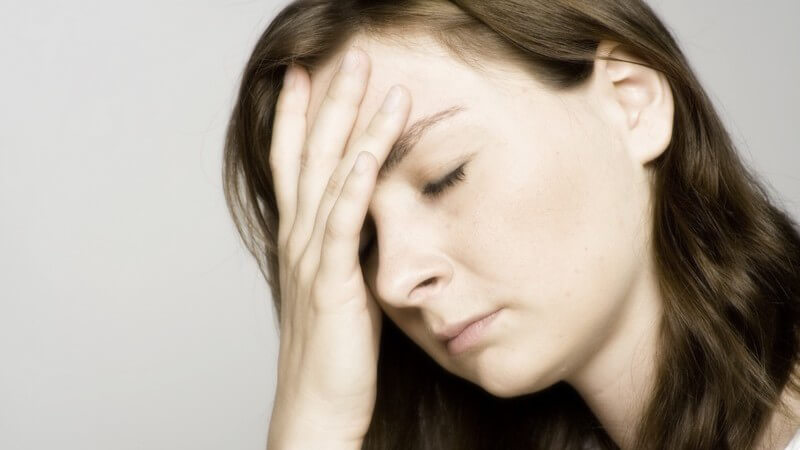 Junge, dunkelhaarige Frau mit Kopfschmerzen hält  Hand auf Stirn