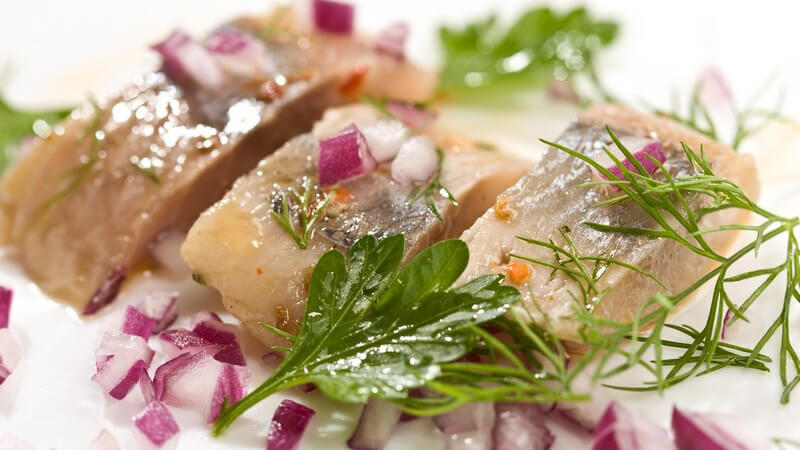 Nahaufnahme Heringsfilet Stücke mit roten Zwiebeln und grünen Kräutern