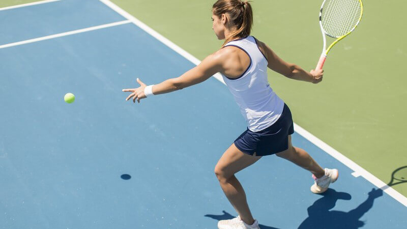 Tennisspielerin holt zum Vorhandschlag auf blauem Hartplatz aus