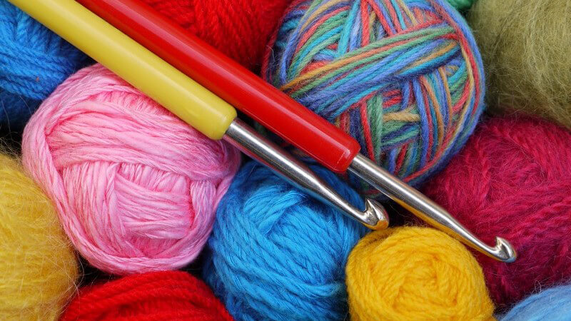 Rote und gelbe Häkelnadel liegen auf einem Haufen verschiedenfarbiger Wollknäuel