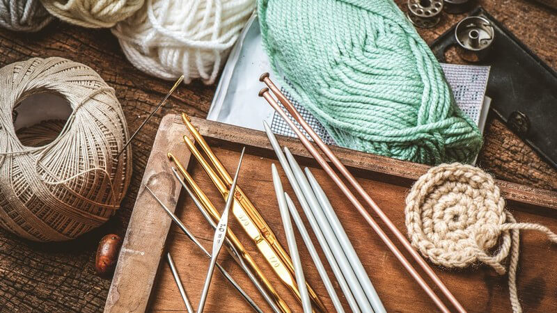 Verschiedene Stricknadeln auf einem Tisch neben Garn, Wolle und Knöpfen