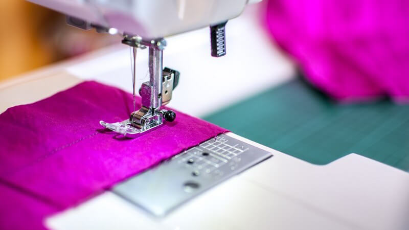 Nähmaschine näht eine Naht in ein Stück lila Stoff