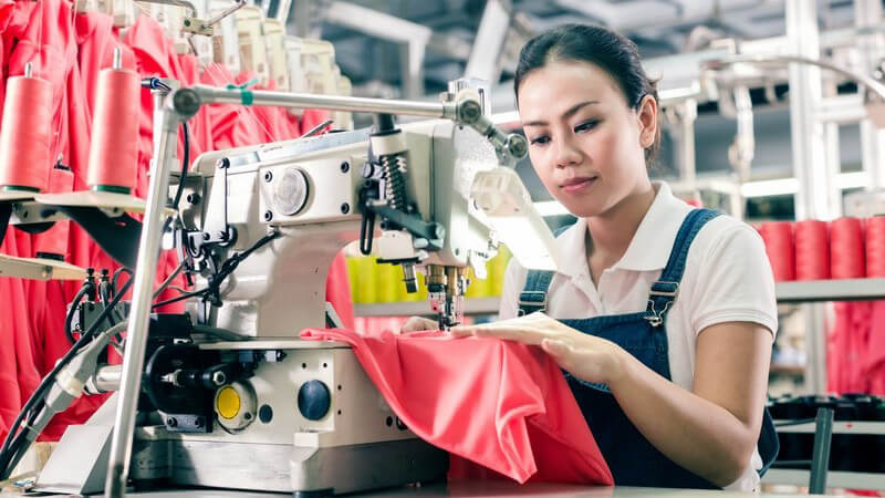 Asiatische Arbeiterin näht roten Stoff mit einer Nähmaschine in einer Textilfabrik