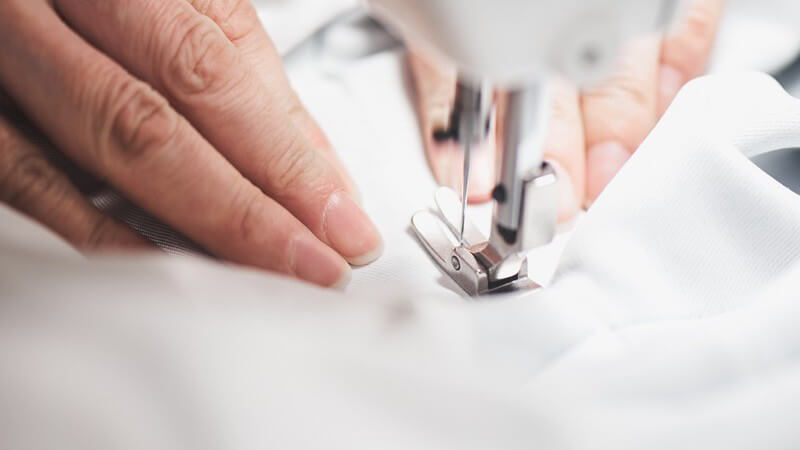 Feiner weißer Stoff gleitet durch eine moderne Nähmaschine