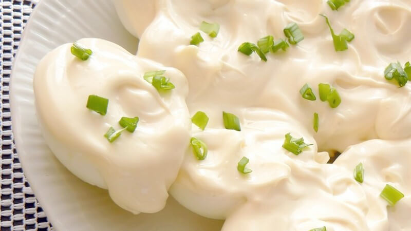 Halbe Eier mit Mayonnaise auf weißem Porzellanteller auf Tischdecke mit Schnittlauch und Kräutern